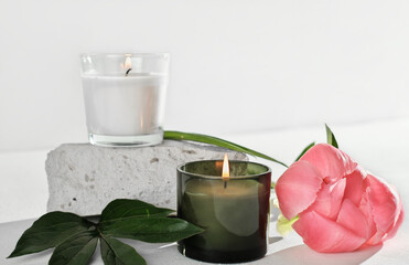 natural soy wax candles next to peony flower and white textured stone. burning candles, home scents and fragrances for calm and peaceful mood.