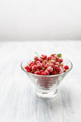 Frozen red currants in a glass vase on a white wooden table. Close-up.