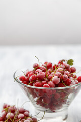 Frozen red currants in a glass vase on a white wooden table. Close-up.