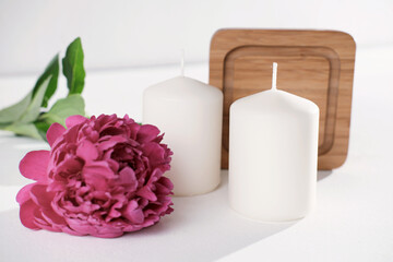 white candles and peony flower on white background. cozy home, house decoration with candles for good mood and atmosphere.