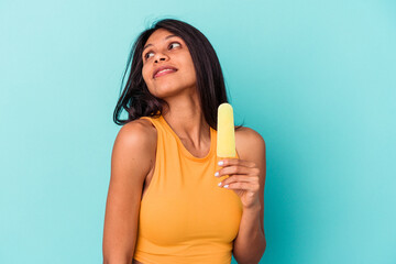 Young latin woman holding ice cream isolated on blue background dreaming of achieving goals and purposes