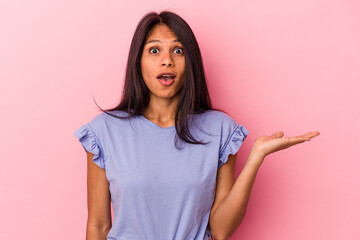 Young latin woman isolated on pink background impressed holding copy space on palm.