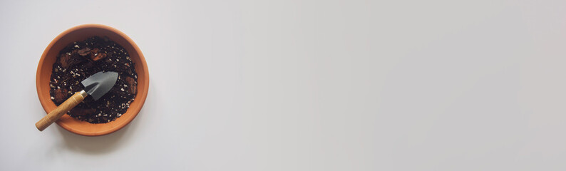 Overhead shot of terracotta pot filled with organic potting soil with a small garden shovel. Isolated on a white background, text space. Concepts for planting, home gardening hobby, Plant parent.