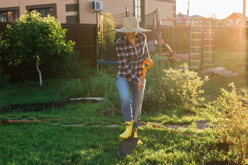 Positive female gardener digs the beds with shovel on sunny warm spring day. Plant care and...