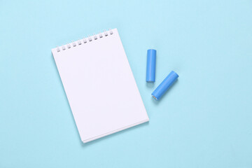 Notebook with aa batteries on blue background. Top view