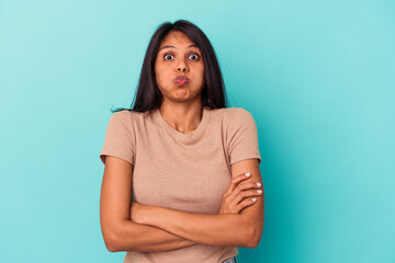 Young latin woman isolated on blue background blows cheeks, has tired expression. Facial expression...
