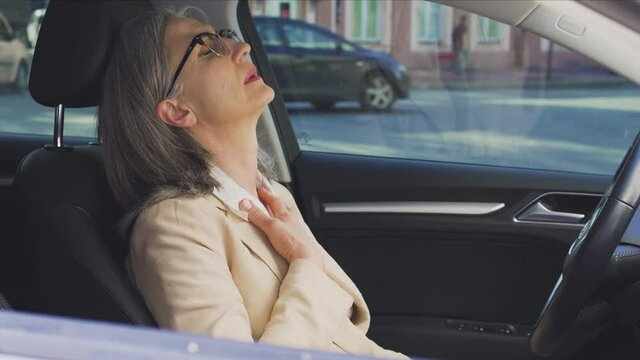 Adult gray haired woman feeling sick sitting in car at parking lot, menopause