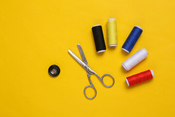 Skeins of colored thread, scissors and button on yellow background
