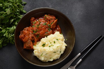 Stewed beef pieces in sauce with mashed potatoes and herbs on dark background