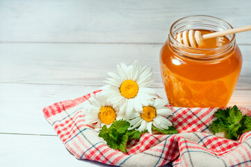 honey in a transparent jar on a wooden background with daisies and strawberries. High quality photo