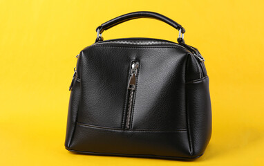 Stylish black leather handbag on yellow background