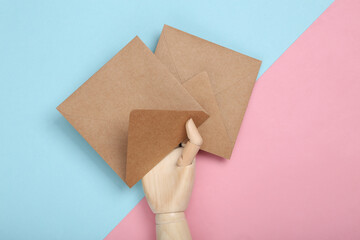 Wooden hand holding craft envelopes on a blue-pink pastel background. Top view
