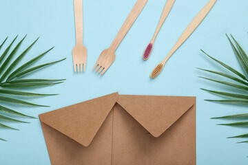 Eco concept. Craft envelope, wooden toothbrushes and forks on blue background with palm leaves