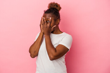Young african american woman isolated on pink background blink through fingers frightened and nervous.