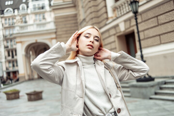 Portrait of a young fashion blonde woman in an autumn trench coat against the background of urban architecture