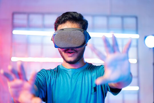 Amazed Young man first time experiencing vr or virtual reality headset on neon light background - concept of futuristic and modern technology.