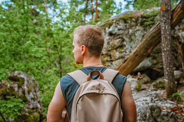 Young man hiking through a pine forest with huge rocks covered with moss