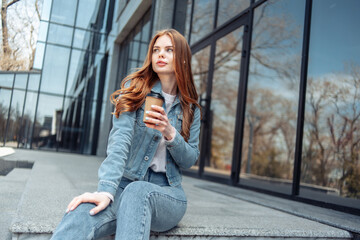 Young pretty woman sits on the stairs near the business center and drinks coffee