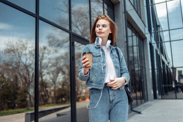 Young beautiful woman in denim jacket and holding coffee cup near the windows of the business center