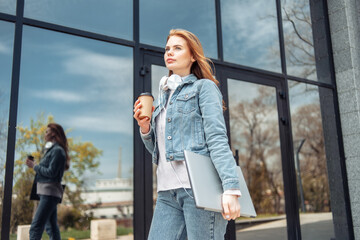 Young woman with laptop and coffee cup stands near business center