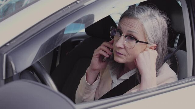 Displeased middle aged woman sitting in car, trying to call to service centre - Powered by Adobe