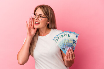 Young russian woman holding bills isolated on pink background shouting and holding palm near opened...