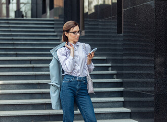 Modern business woman uses a smartphone while standing on the stairs