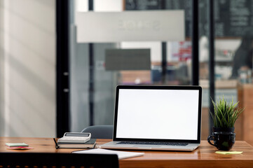 Mockup blank screen laptop computer and supplies on wooden table in modern office room.