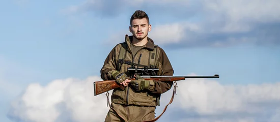  Hunter with hunting gun and hunting form to hunt sky background. Hunter is aiming. Hunter man. Shooter sighting in the target. Hunting period © Yevhen