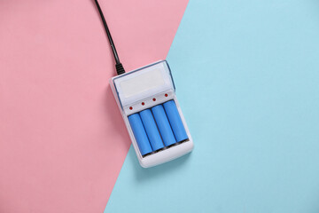 Battery charger with AA rechargeable batteries on blue pink pastel background