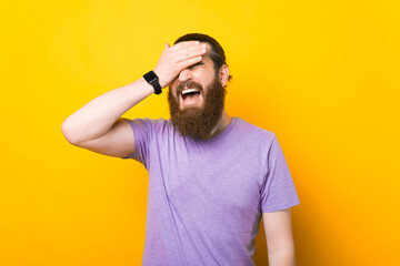 Bearded man is making a face palm in a studio over yellow background.