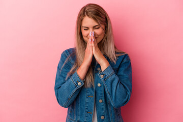 Young russian woman isolated on pink background holding hands in pray near mouth, feels confident.