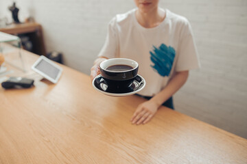 Female barista offering cup of coffee in cafeteria