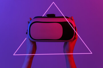 Hands holding vr headset in neon gradient light with triangle