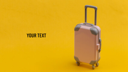 Travel or trip concept. Mini pink plastic travel suitcase on yellow background. Minimal style. Copy space
