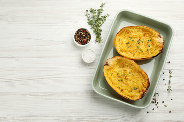 Halves of cooked spaghetti squash in baking dish, thyme and spices on white wooden table, flat lay. Space for text
