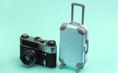 Travel or trip concept. Mini plastic travel suitcase and camera on blue pastel background. Minimal style