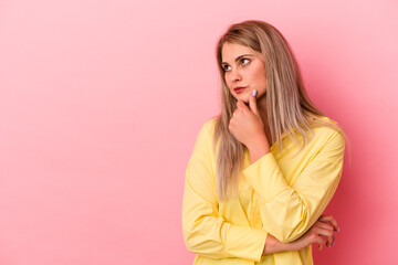 Young russian woman isolated on pink background looking sideways with doubtful and skeptical expression.