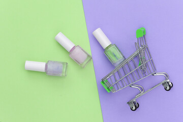 Shopping trolley with nail polish bottle on green purple background. Beauty market. Top view