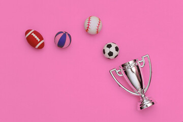 Mini different sports balls and champion cup on pink background. Minimalism Sport concept. Top view. Flat lay.
