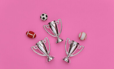 Mini different sports balls and champion cups on pink background. Minimalism Sport concept. Top view. Flat lay.