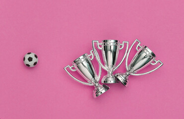 Mini soccer ball and championship cups on pink background. Minimalism Sport concept. Top view. Flat lay
