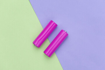 Two yellow AA batteries on green purple pastel background. Top view