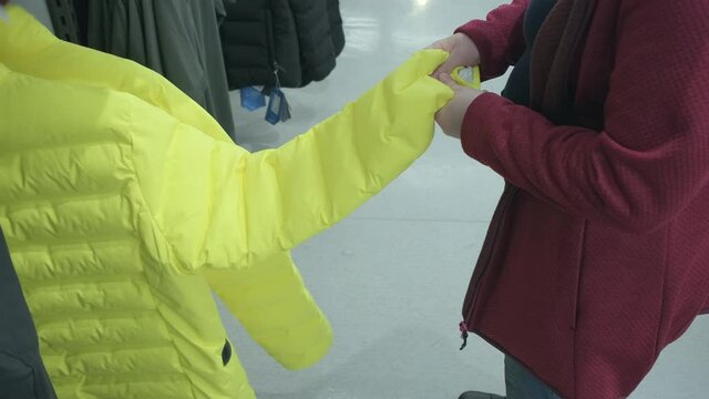 Caucasian pregnant woman chooses a yellow warm jacket on a sintepon in store to buy. Concept of buying new clothes, fashion, beauty and an active lifestyle while carrying child. Hands close up shot