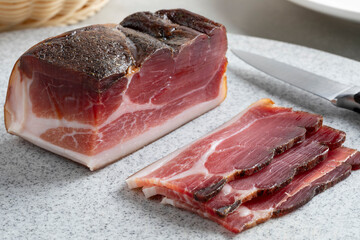 Piece of German Sudtiroler speck and slices on a cutting board close up 