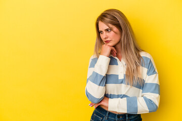 Young russian woman isolated on yellow background looking sideways with doubtful and skeptical expression.