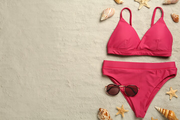 Stylish bikini and beach accessories on sand, flat lay. Space for text