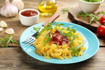 Tasty spaghetti squash with tomato sauce and arugula served on wooden table
