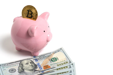 Bitcoin piggy bank and pack of hundred dollar bills spread out on white background.