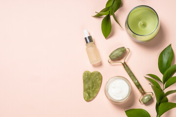 Plakat Cosmetic products - Jade roller and gua sha massager with cream and serum bottles at pastel background. Spa background. Top view with copy space.